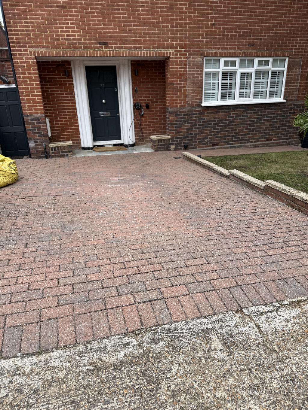 Front paved driveway beside the garage with a tidier, more even paving appearance and reduced debris and weeds across the surface.